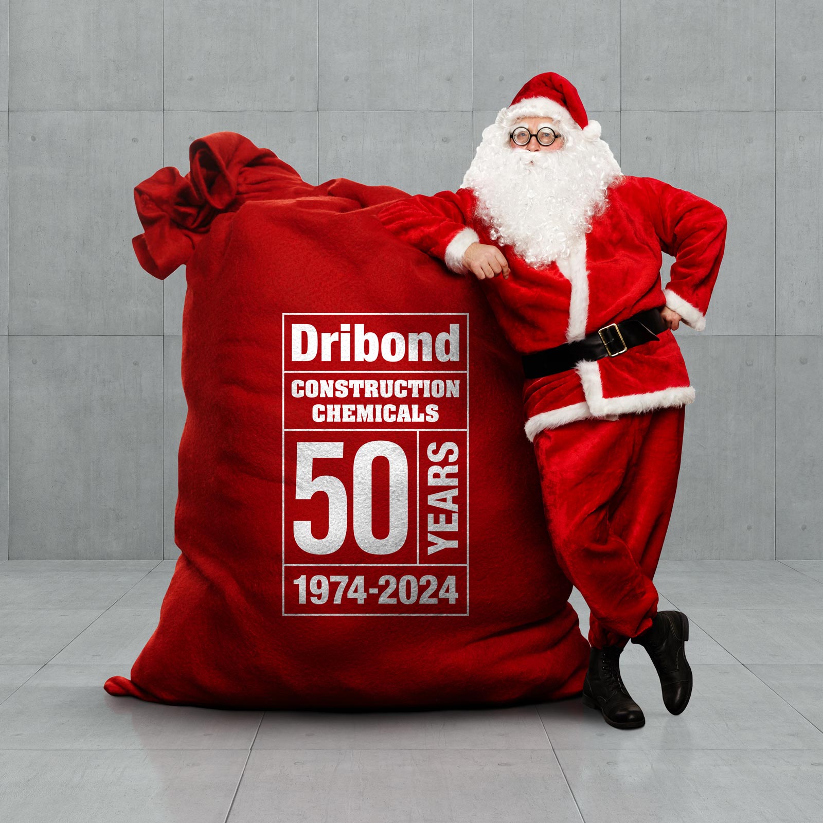 Santa leaning against a large red sack with white logotype: Dribond Construction Chemicals – 50 Years, 1974-2024